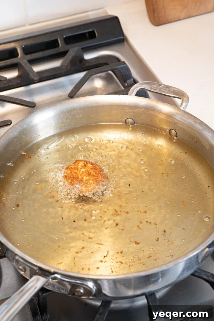 Golden Ham Croquettes 10 A croqueta being fried to a perfect golden brown in hot oil, showcasing the crisping process.
