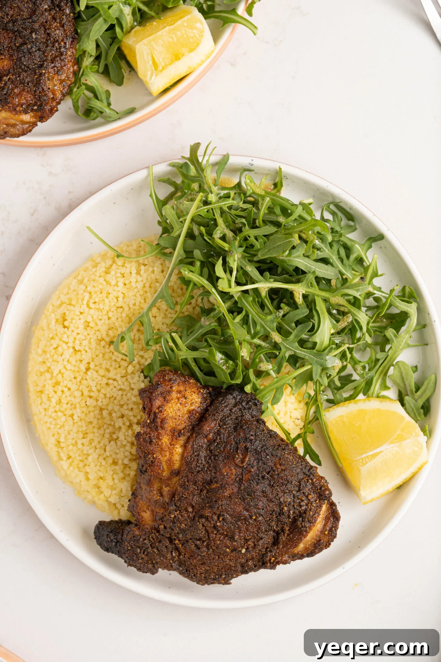 Effortless Ras El Hanout Chicken Thighs Three Ingredients 2 A perfectly roasted Ras el Hanout chicken thigh presented on a plate with fluffy couscous and fresh arugula, highlighting its golden-brown skin and aromatic spices.