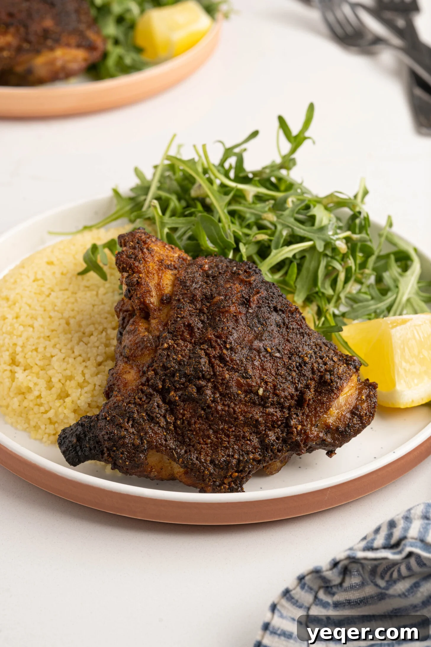 Effortless Ras El Hanout Chicken Thighs Three Ingredients 8 A vibrant plate featuring a perfectly roasted Ras el Hanout chicken thigh, alongside a mound of fluffy couscous and a fresh bed of arugula, illustrating a complete and inviting meal.