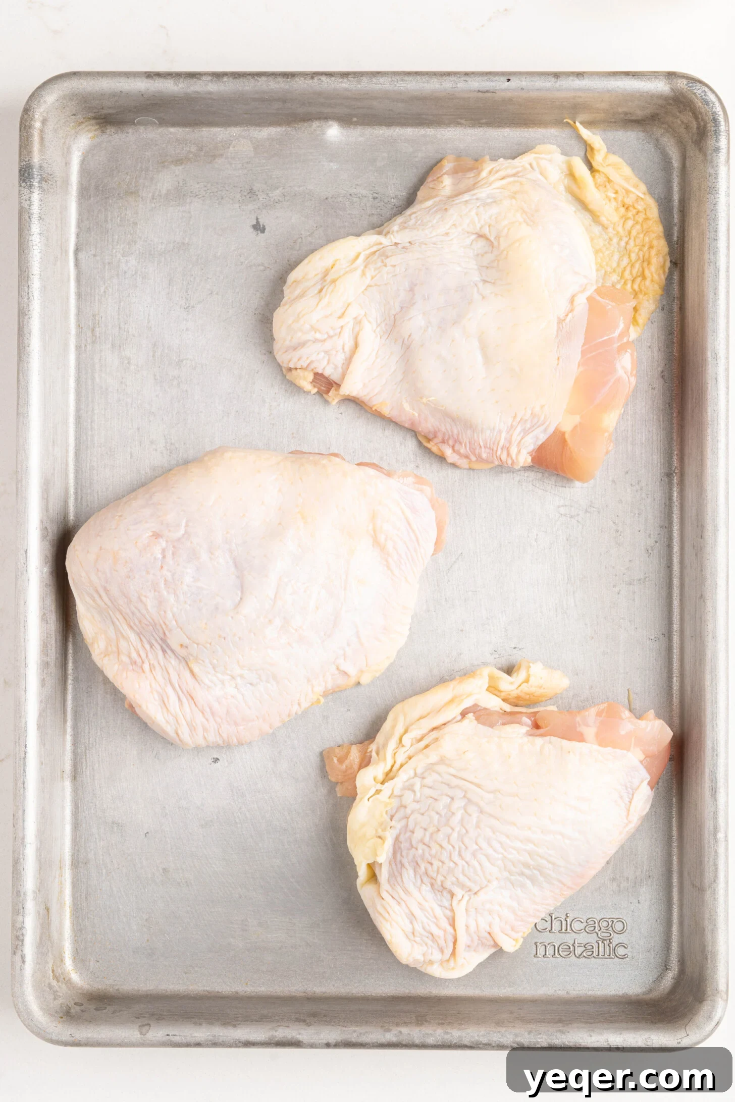 Chicken thighs neatly arranged on a sheet pan, ready for the oven, after being seasoned.