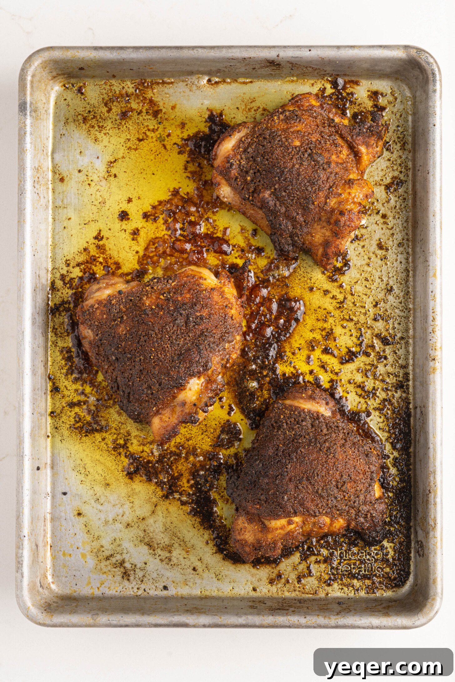 The perfectly baked and seasoned chicken thighs resting on the pan after coming out of the oven.