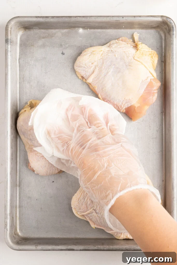 Effortless Ras El Hanout Chicken Thighs Three Ingredients 5 A hand gently pats chicken thighs dry with paper towels on a cutting board, an essential step for achieving crispy skin.