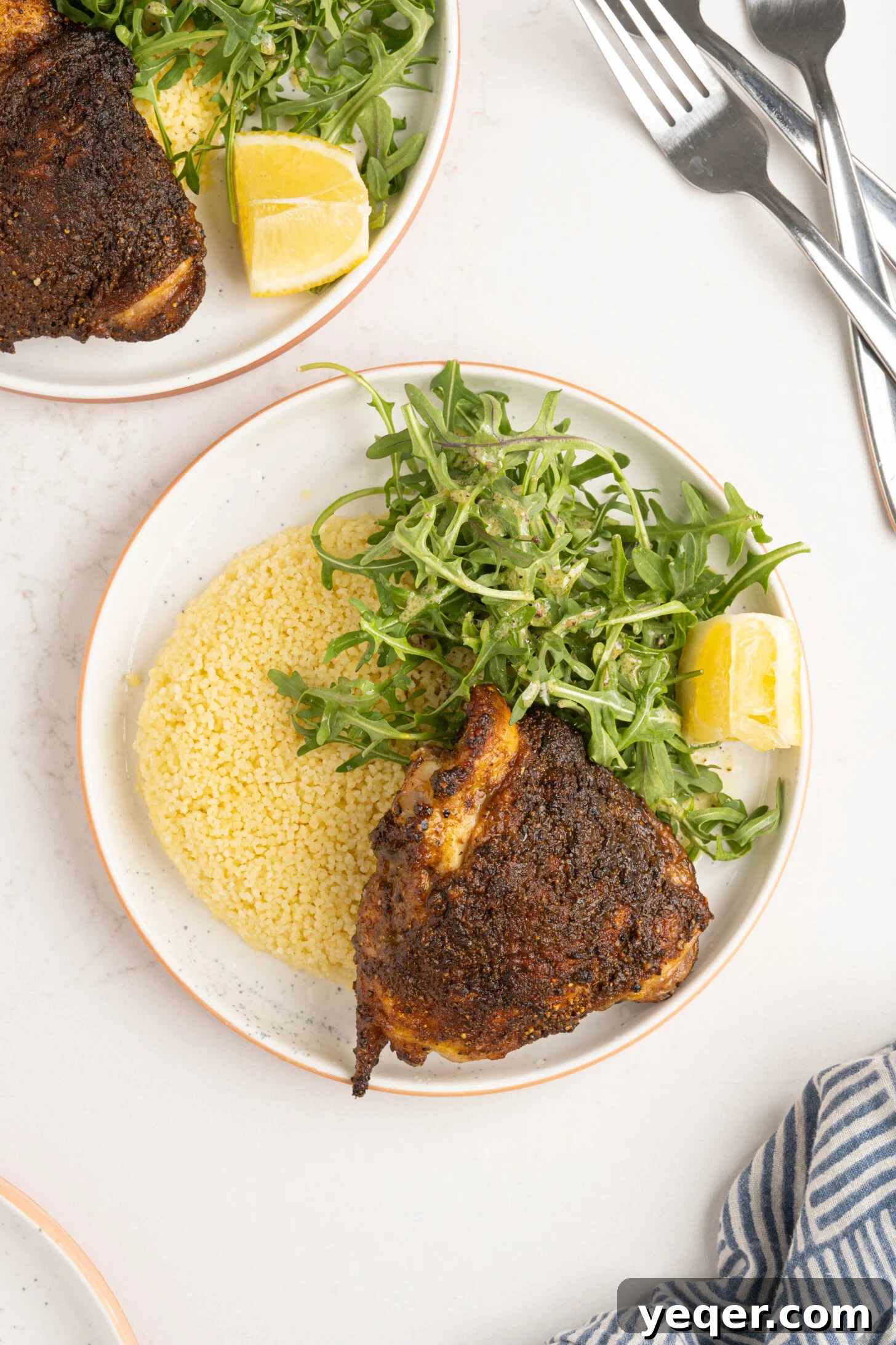 Effortless Ras El Hanout Chicken Thighs Three Ingredients 7 Two plates each hold a succulent Ras el Hanout chicken thigh, accompanied by a side of fluffy couscous and fresh arugula, showcasing a complete and inviting meal.