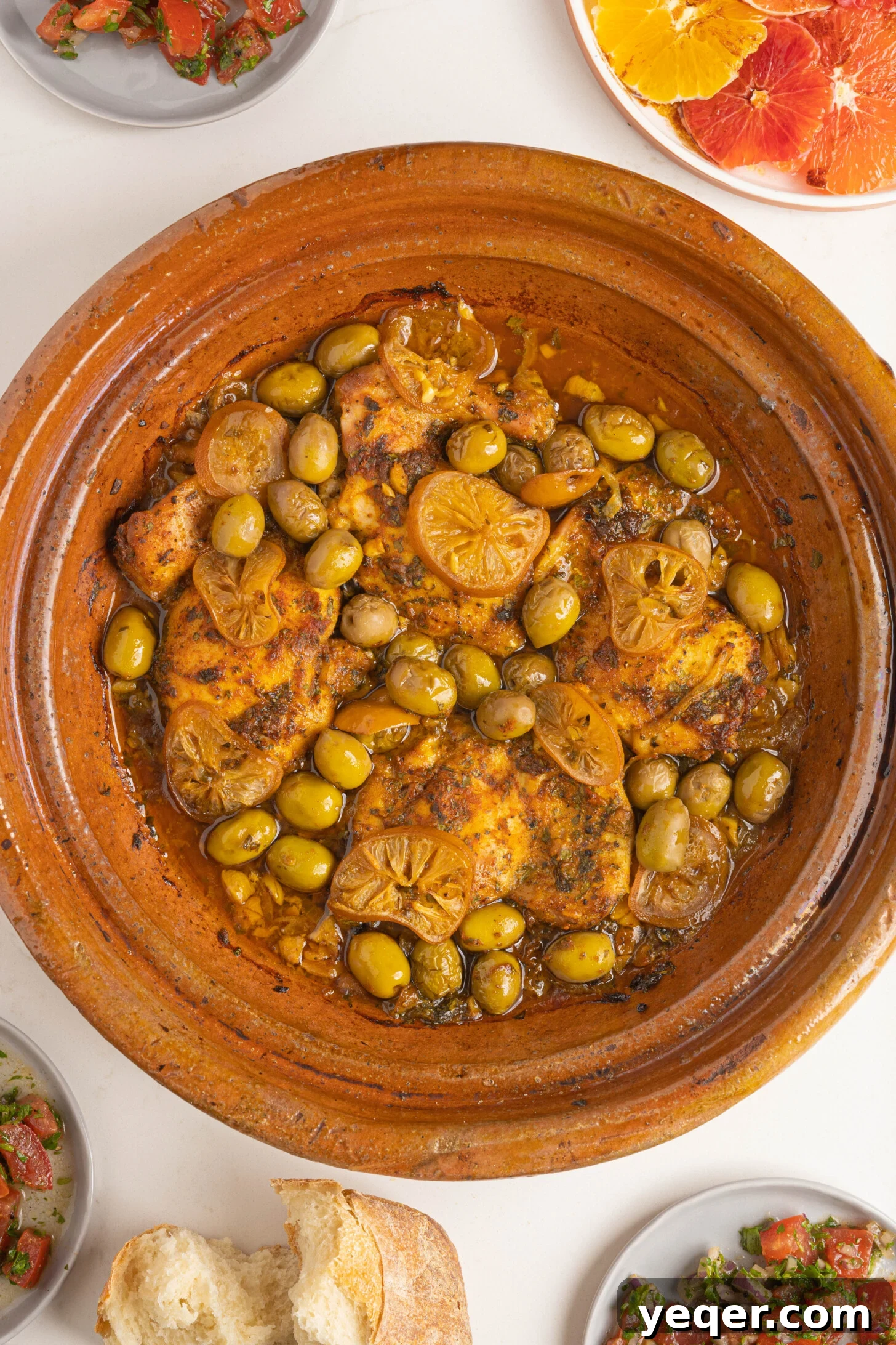 Unveiling the Moroccan Art of Tagine Service 2 A vibrant chicken tagine, surrounded by an array of fresh Moroccan salads and warm bread, ready to be served on a pristine white counter.