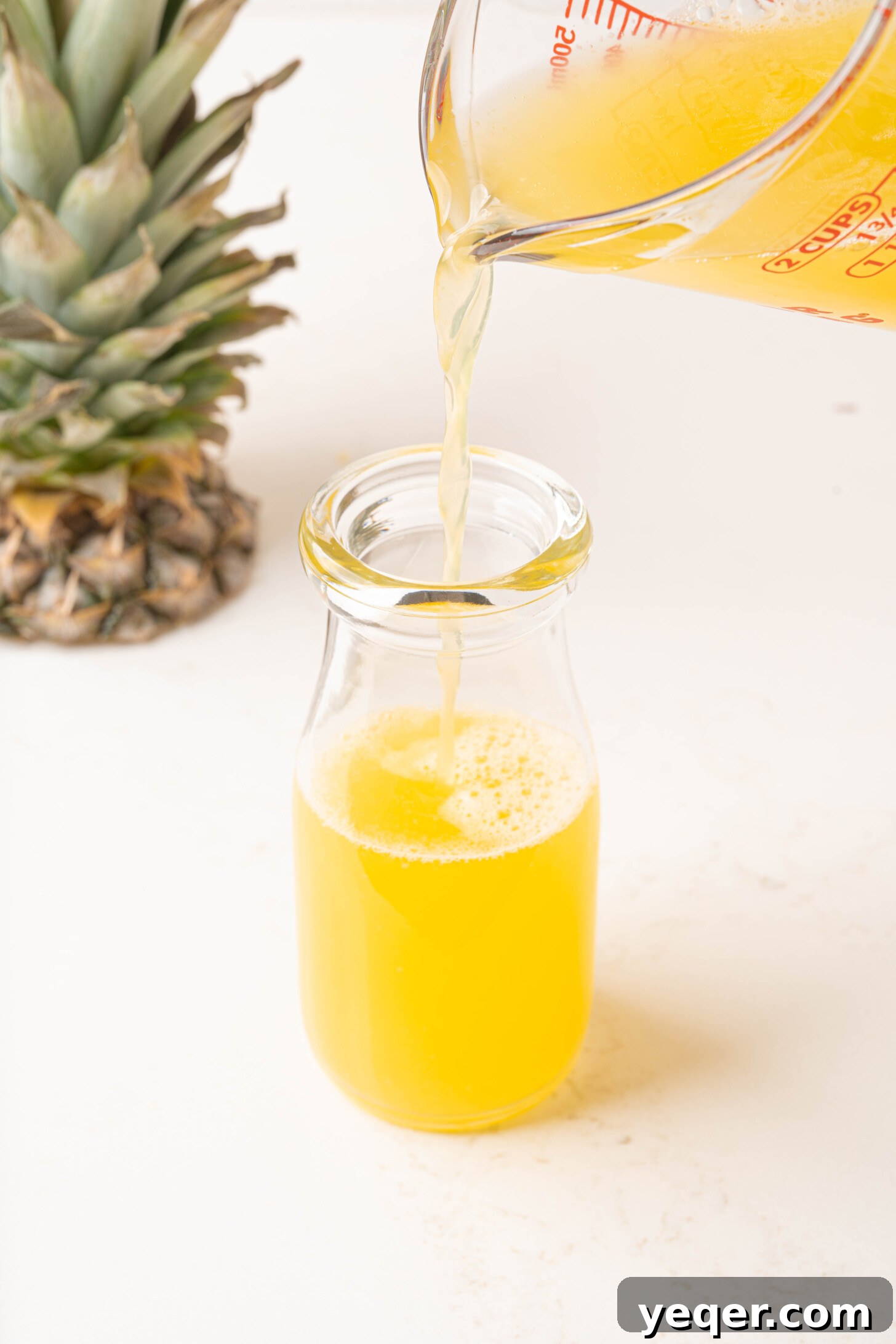 Freshly extracted pineapple juice being poured from a clear blender jug into an elegant glass bottle for storage.