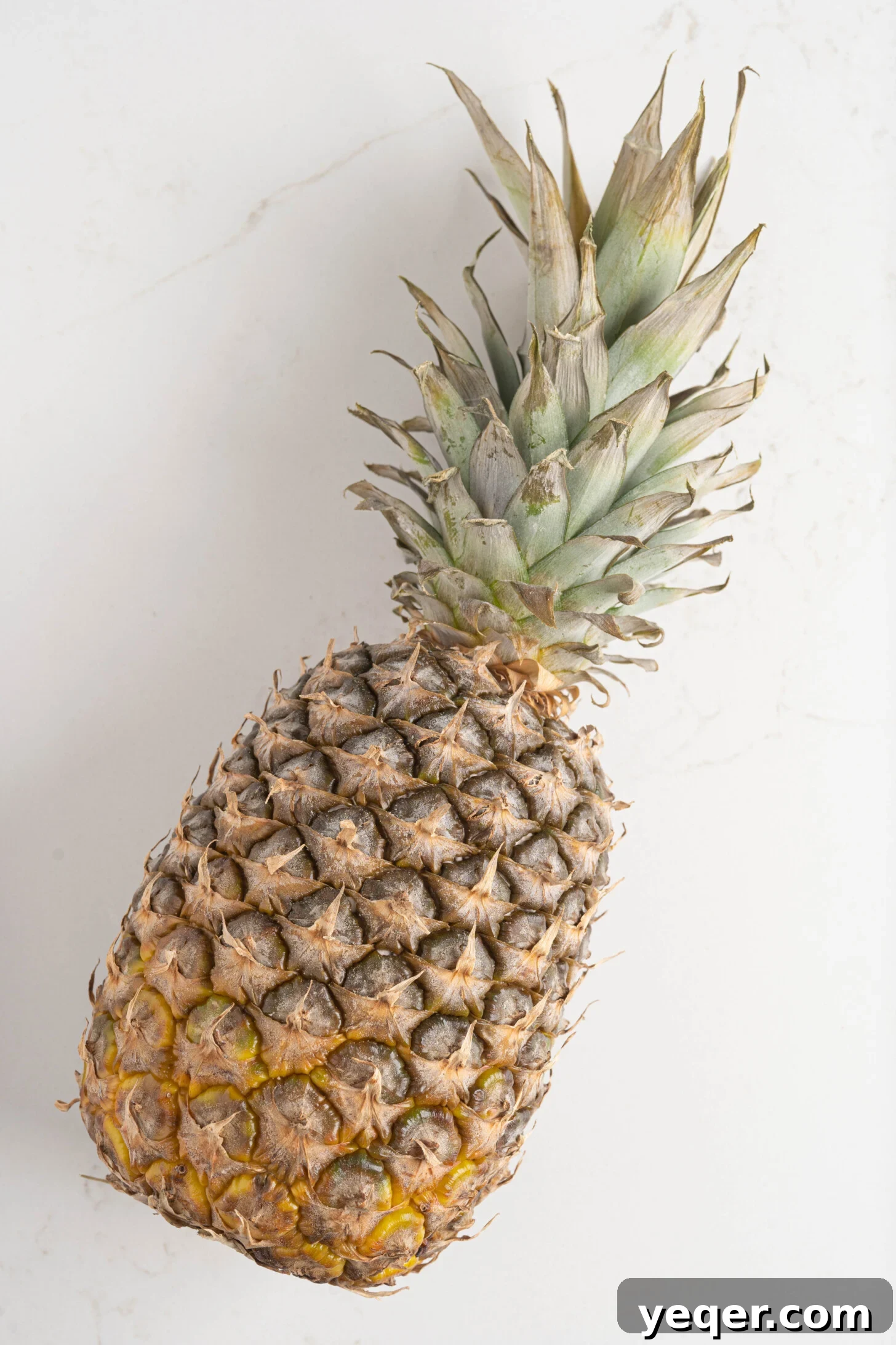 A whole, ripe pineapple resting elegantly on a pristine white kitchen counter, ready for preparation.