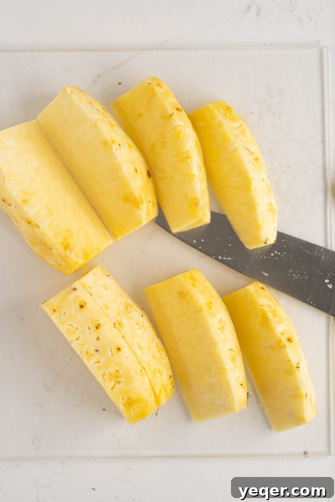 A freshly peeled pineapple, perfectly cut into eight uniform segments, arranged on a rustic wooden cutting board.