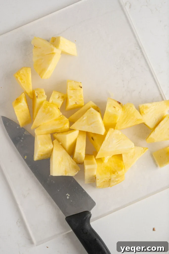 A pile of perfectly chopped pineapple chunks on a wooden cutting board, ready to be transferred to the blender.