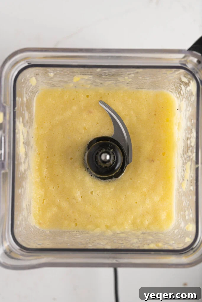 A high-speed blender container filled with thoroughly pureed pineapple, appearing completely liquid and smooth.