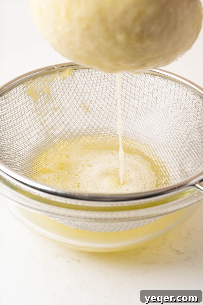 Golden pineapple juice being carefully strained from a cheesecloth into a large glass bowl, separating the liquid from the fibrous pulp.