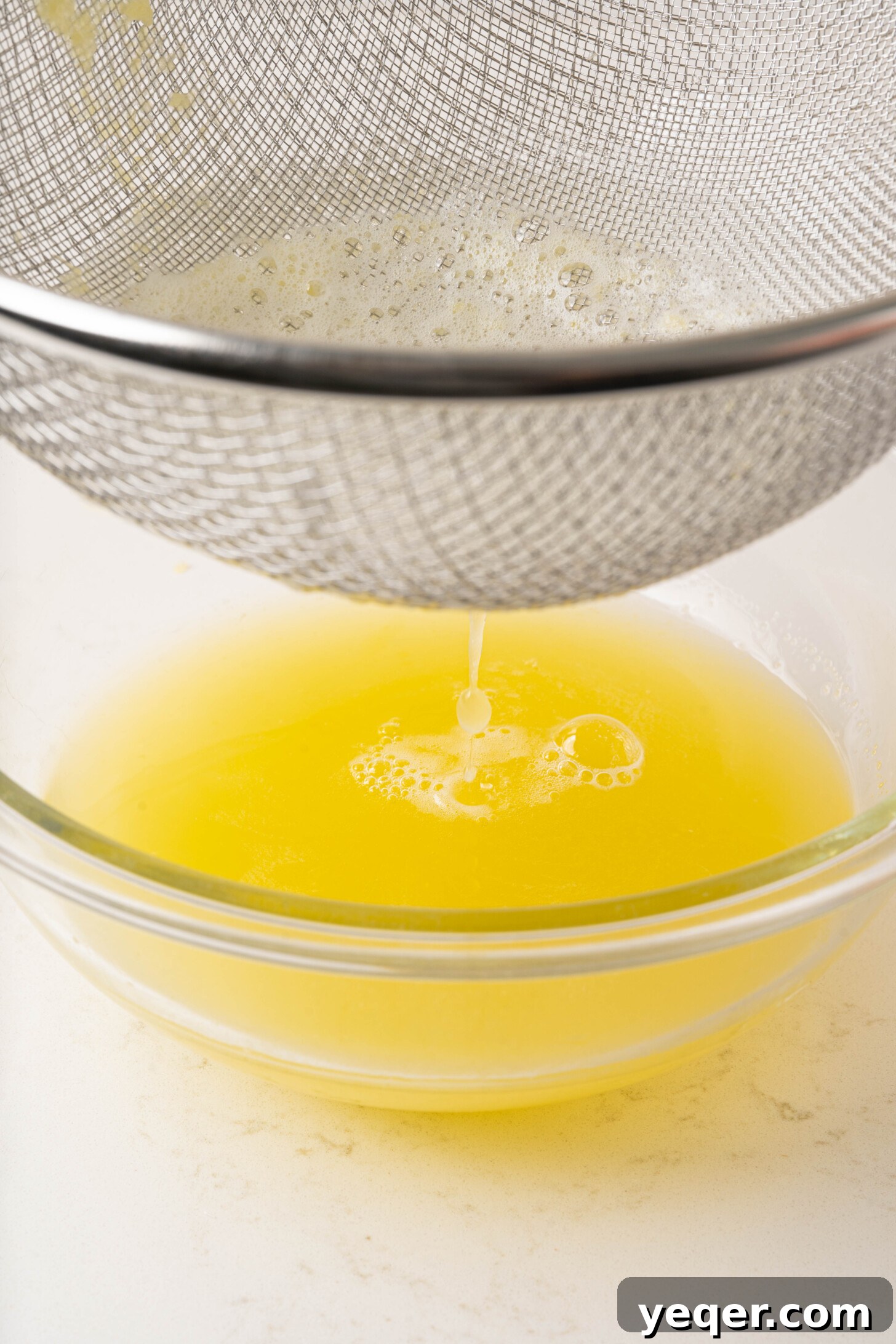 Pure, golden pineapple juice steadily draining into a large clear glass bowl, showcasing its brilliant color and smooth texture.