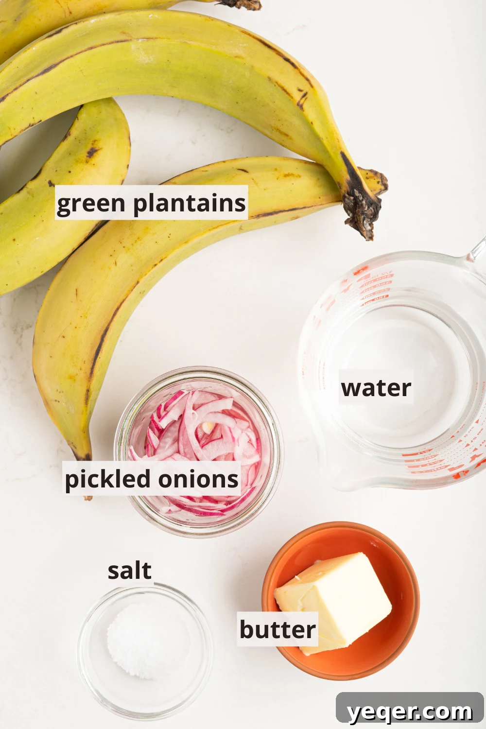 Whip Up Dominican Mangu in 30 Minutes 3 Green plantains, water, red onions, salt, and butter laid out on a table, ready for cooking.