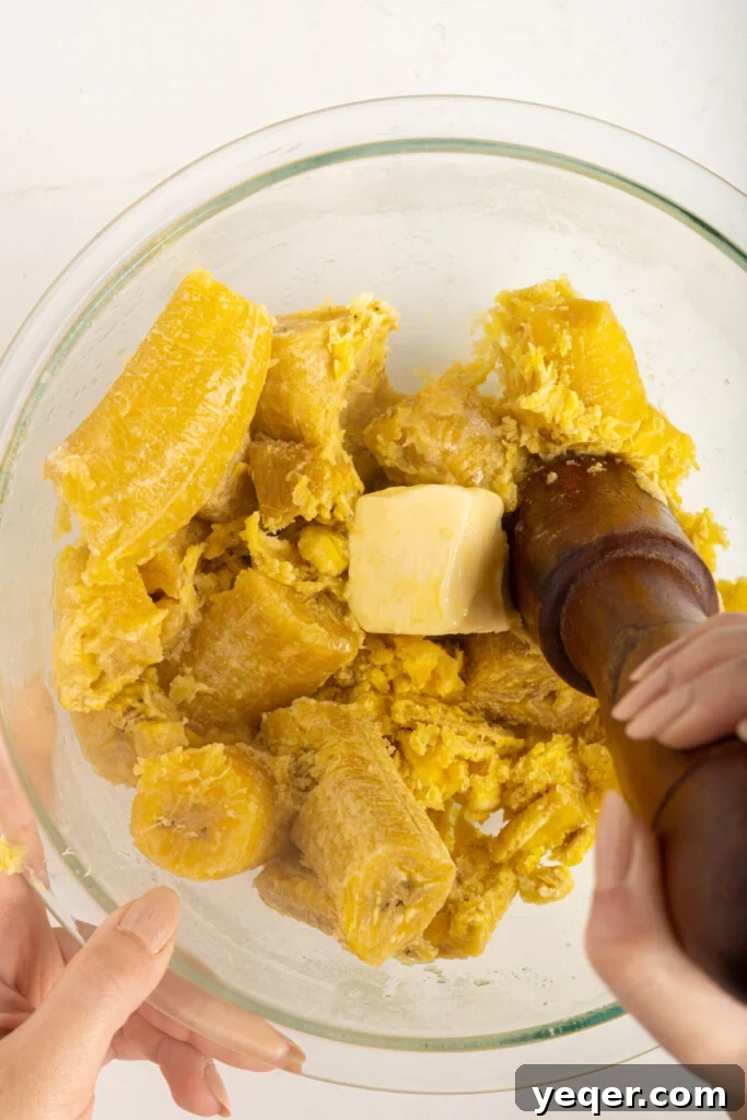 Whip Up Dominican Mangu in 30 Minutes 5 Cooked green plantains being mashed in a bowl with butter, showing a creamy texture.