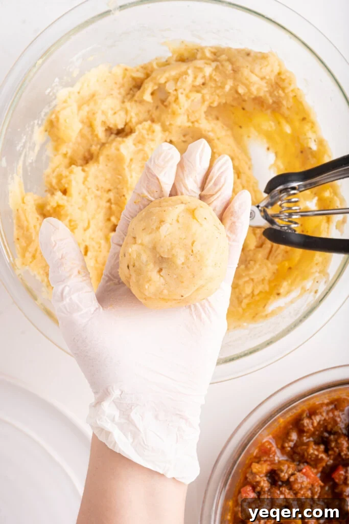 Golden Crispy Stuffed Potatoes 11 A hand carefully shaping the mashed potatoes around the picadillo filling to form a uniform croquette.