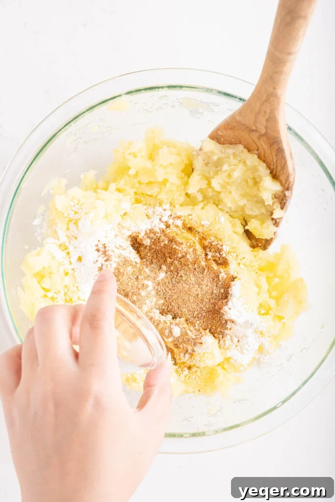 Golden Crispy Stuffed Potatoes 8 A hand adding a spoonful of seasonings to a bowl of freshly mashed potatoes.