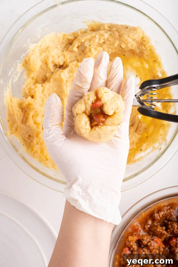 Golden Crispy Stuffed Potatoes 10 Papas Rellenas being carefully formed in a hand, with the picadillo filling visible in the center of the potato ball.
