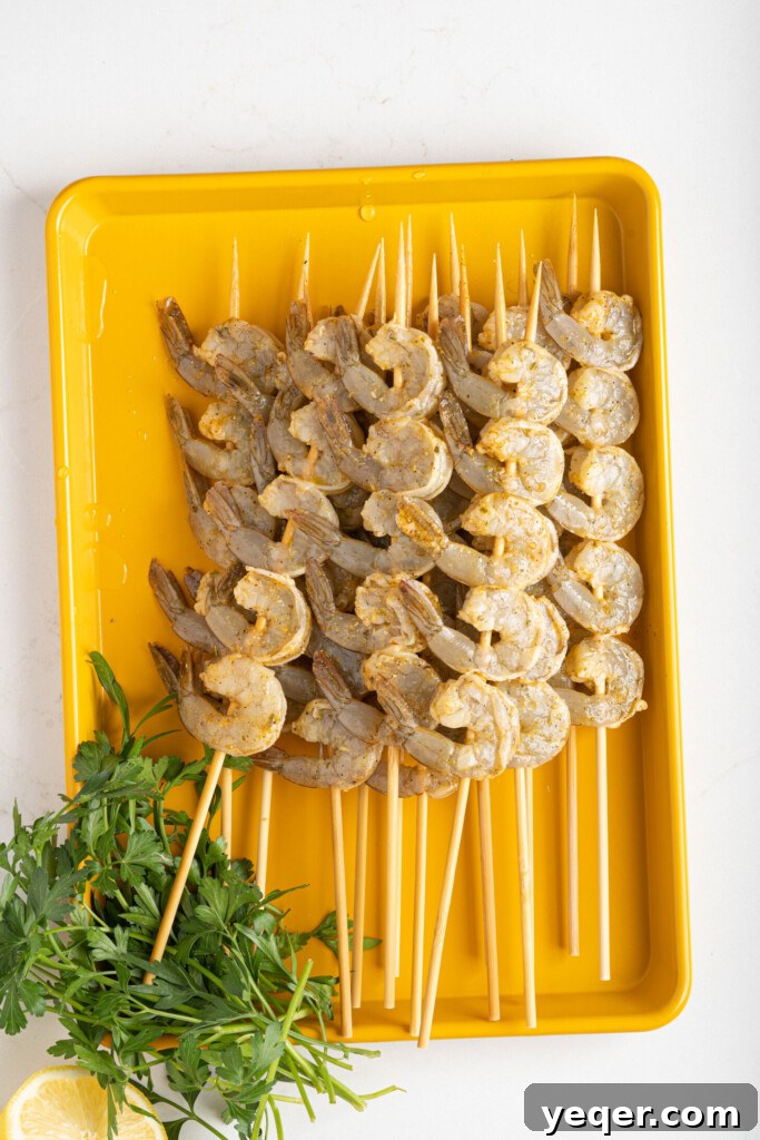 Simply Delicious 5 Ingredient Grilled Shrimp Skewers 6 Several raw, marinated shrimp carefully threaded onto wooden skewers and laid out on a baking sheet, ready for the grill.