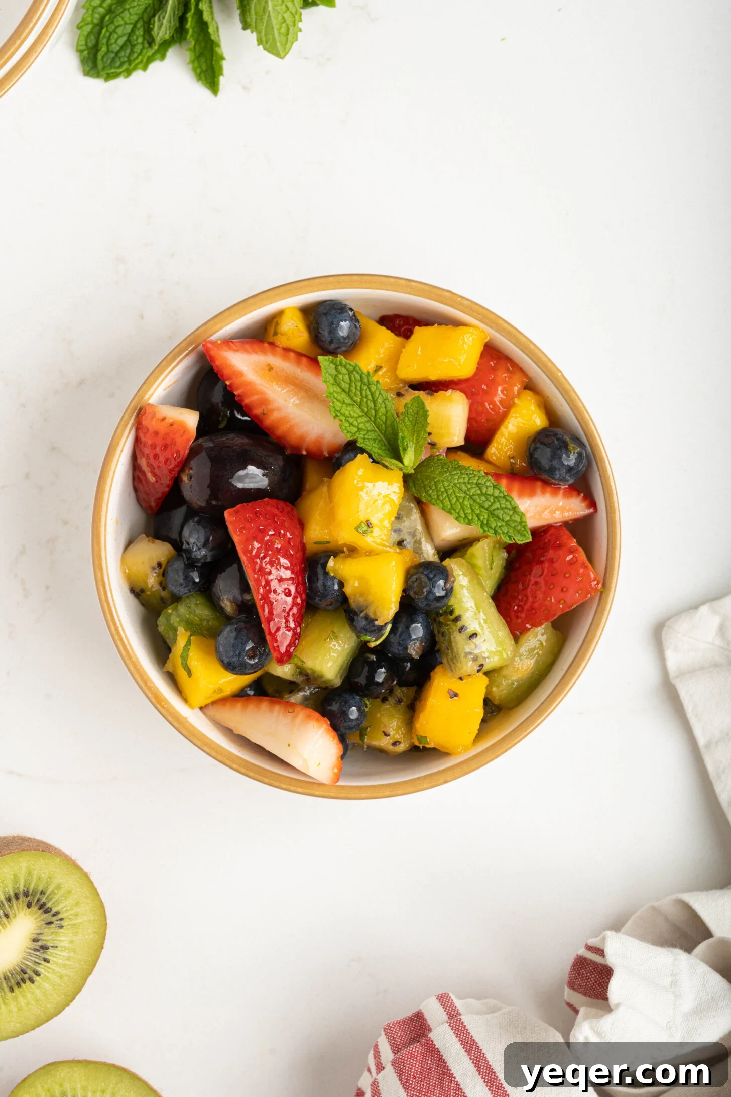 A beautifully arranged classic fruit salad in a pristine white bowl, showcasing vibrant colors of various fresh fruits like strawberries, blueberries, kiwi, mango, and grapes, garnished with fresh mint leaves.