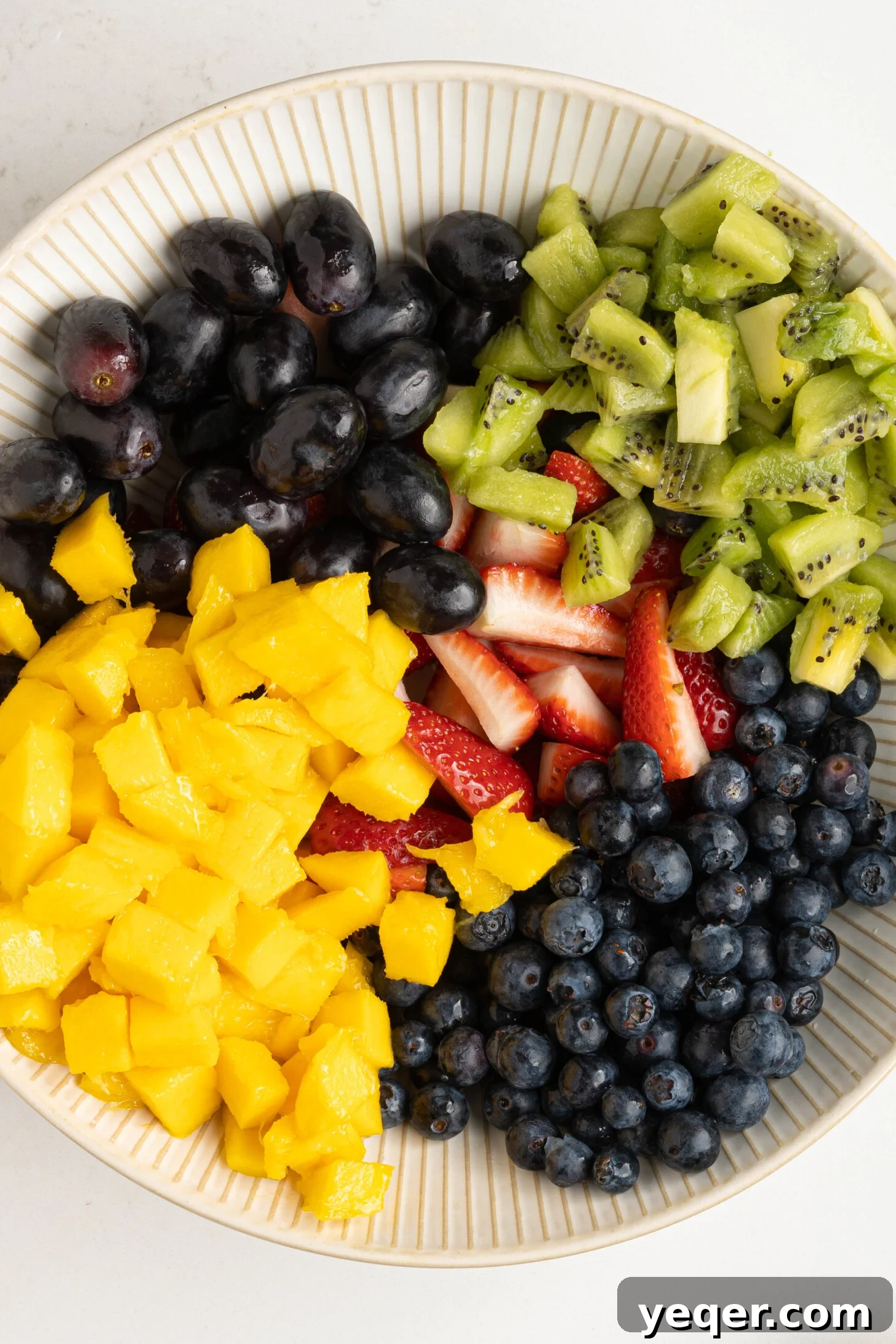 A white bowl brimming with an artistic arrangement of assorted fresh fruits, showcasing a variety of colors and textures.