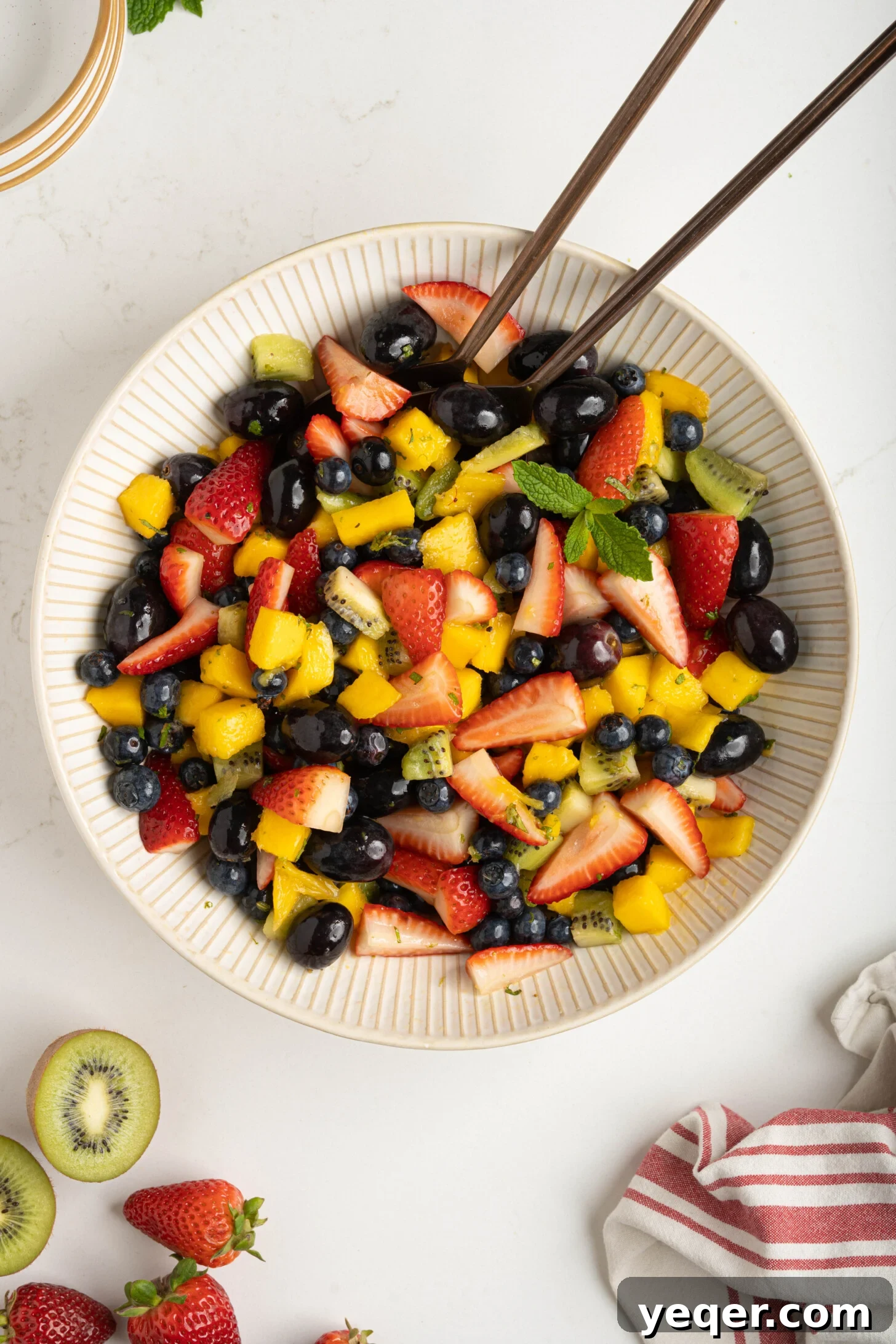 A close-up shot of the colorful fruit salad in a white bowl, highlighting the fresh mint and lime zest scattered over the diced fruits.