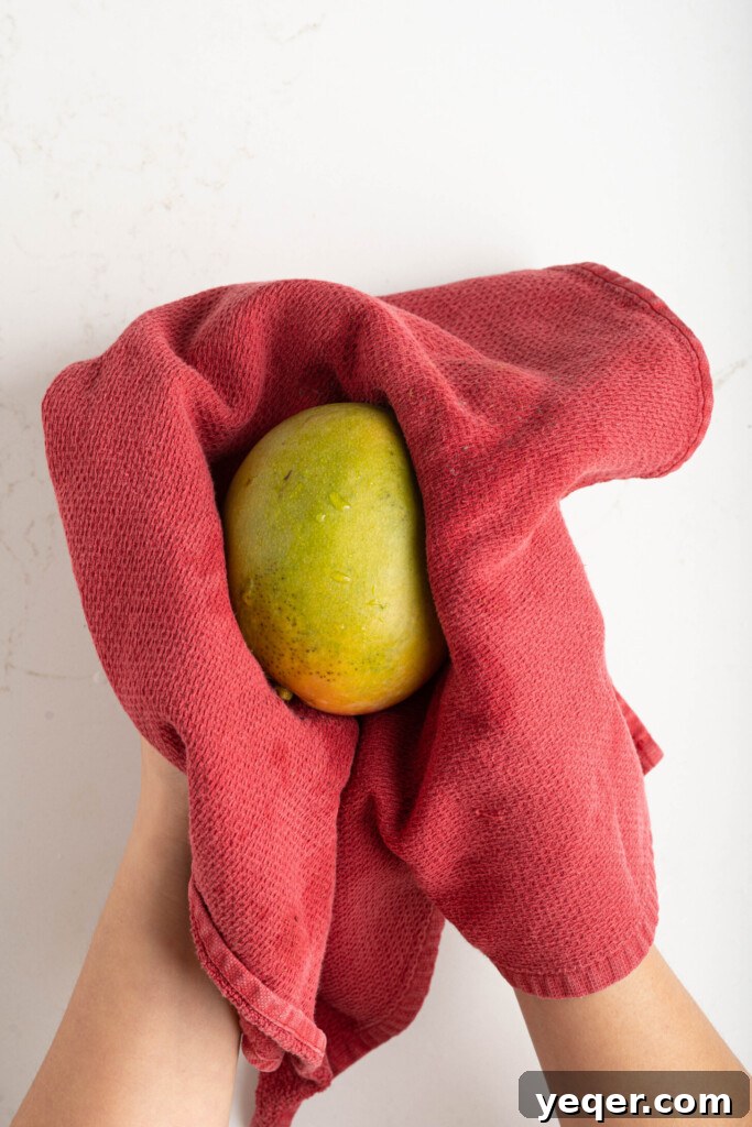 A close-up of a mango being dried meticulously with a white towel, emphasizing the importance of removing excess moisture.