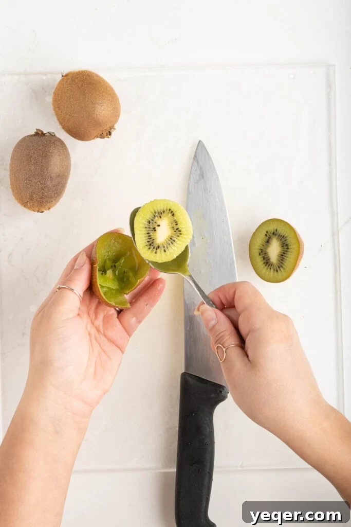 A kiwi being easily peeled by scooping out its flesh with a spoon after being cut in half.