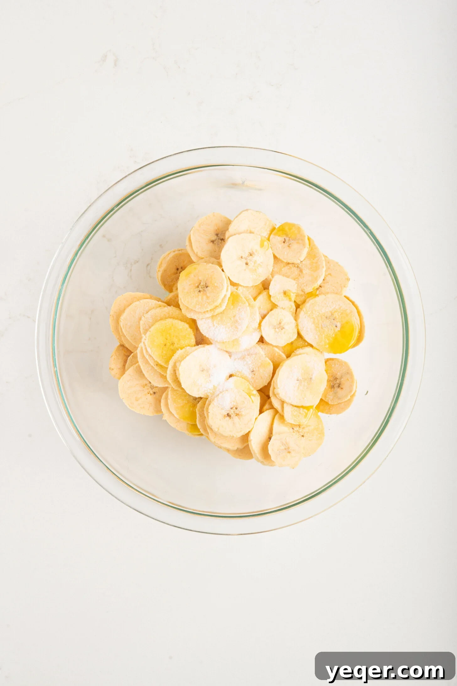 Effortless Oven-Baked Plantain Crisps 8 A bowl of thinly sliced raw plantain chips coated in oil and salt, ready for baking.