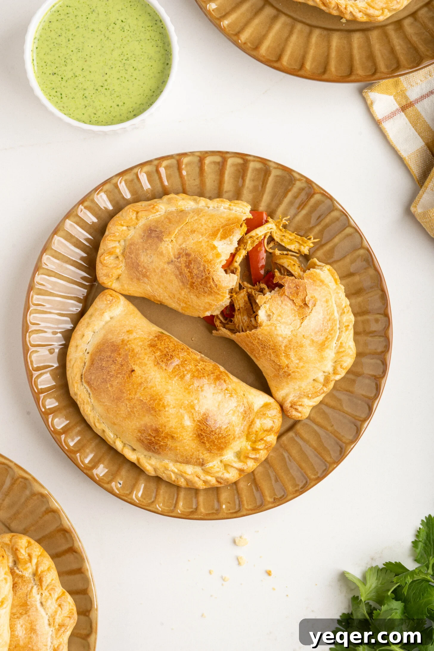 Homestyle Shredded Chicken Empanadas 12 An appetizing overhead view of two chicken empanadas, one perfectly crimped with a fork and the other with a hand-folded edge, showcasing different sealing techniques.