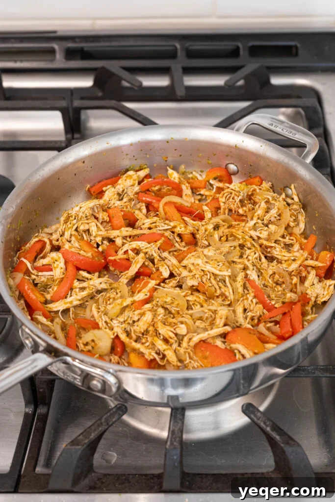 Homestyle Shredded Chicken Empanadas 6 A pot showing shredded chicken mixed with sofrito, onion, and bell pepper, simmering with seasonings and tomato paste.