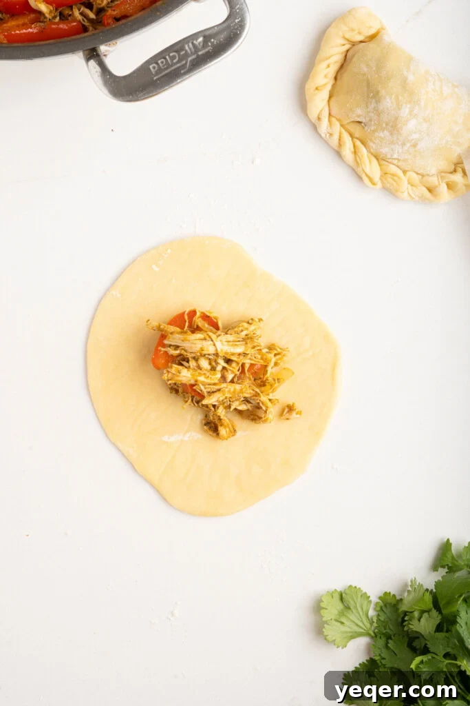 Homestyle Shredded Chicken Empanadas 7 An empanada dough disc partially folded over with a spoonful of chicken filling perfectly centered, ready for sealing.