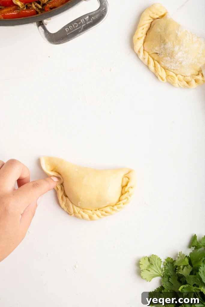 Homestyle Shredded Chicken Empanadas 8 A close-up shot of a hand expertly crimping the edges of an empanada using a fork, creating a neat seal.