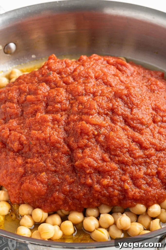 Hearty 30-Minute Moroccan Chickpea and Tomato Stew 5 Chickpeas and crushed tomatoes being added to sautéed onions and spices in a pan.