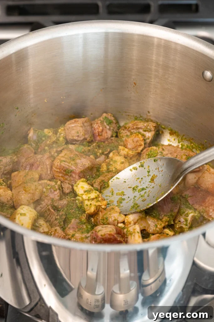 Rich Puerto Rican Sancocho Beef and Root Vegetable Stew 5 Meat browning in a pot with sofrito, stirred with a wooden spoon to ensure even cooking and caramelization.