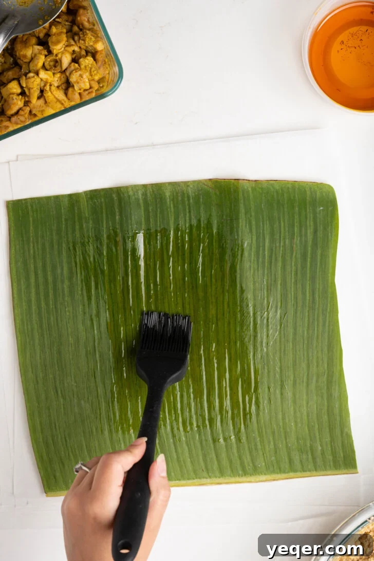 Puerto Rican Pasteles: Savory Meat-Stuffed Masa Delights 13 A banana leaf being gently brushed with achiote oil on a piece of parchment paper.