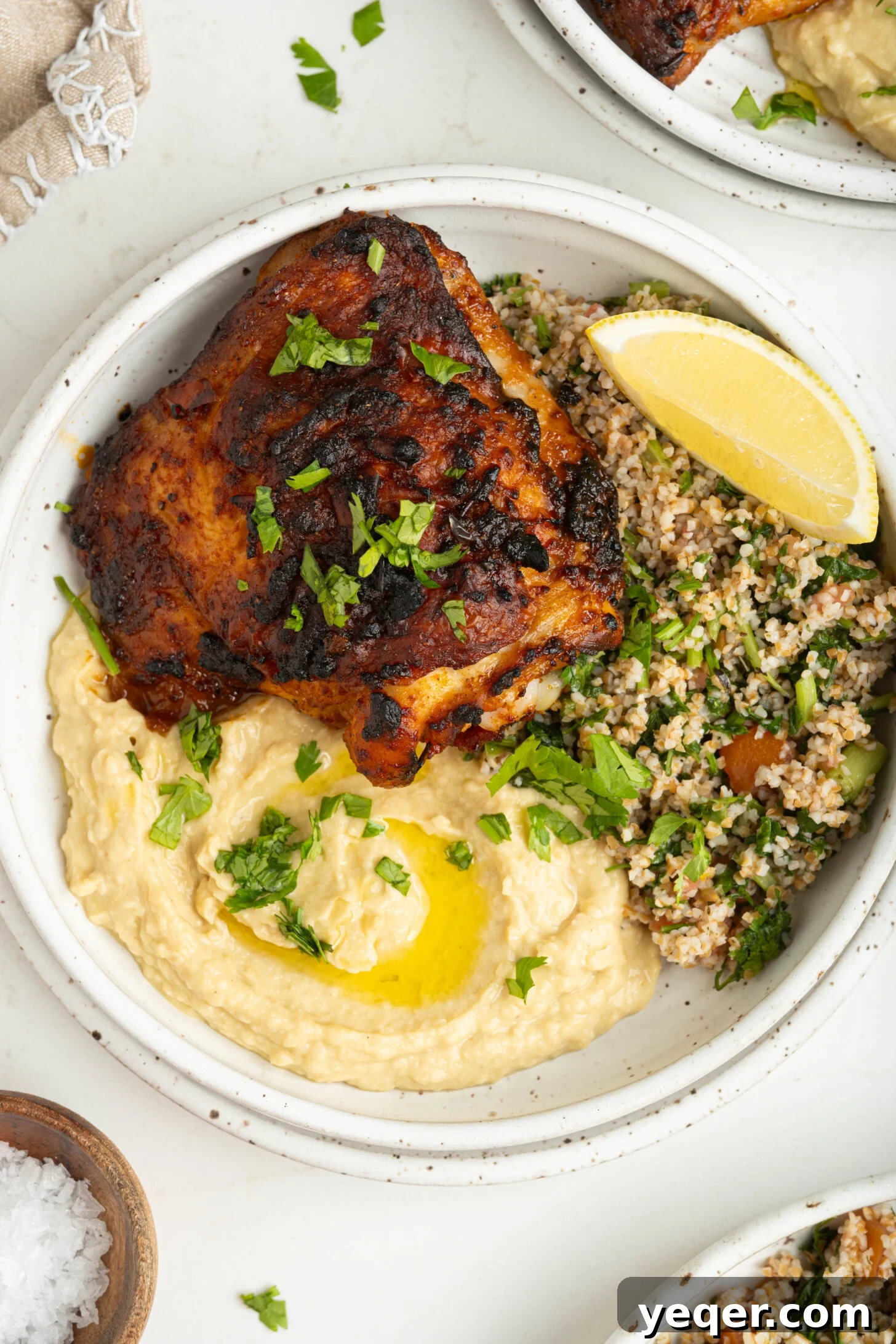 Fast & Flavorful Harissa Roasted Chicken Thighs 9 A single, perfectly roasted harissa chicken thigh, glistening with marinade, served elegantly alongside creamy hummus and a fresh, vibrant green salad.