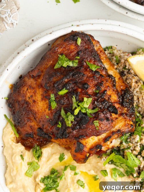 a bowl with a chicken thigh, hummus, and salad