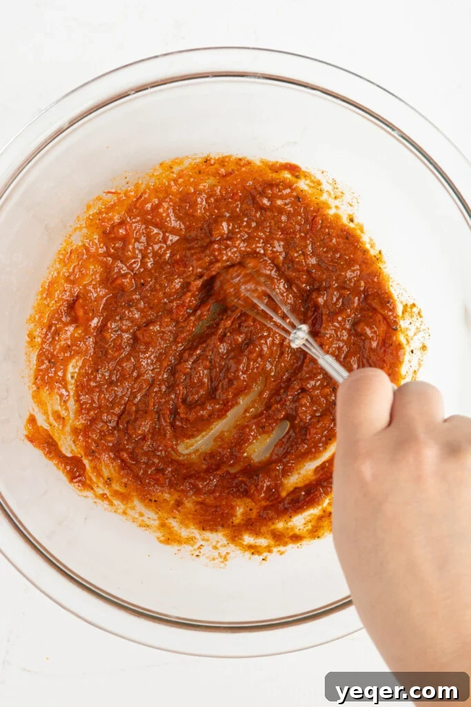 Fast & Flavorful Harissa Roasted Chicken Thighs 4 A vibrant red harissa marinade being meticulously mixed in a bowl, showcasing the rich colors and textures of the ingredients combining.