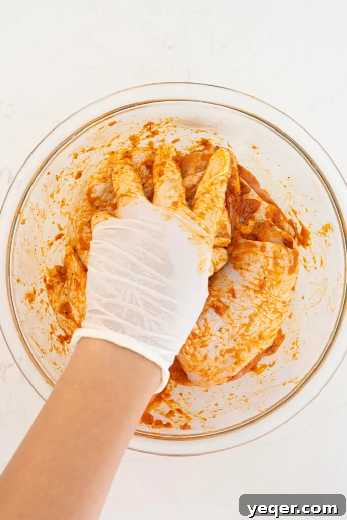Fast & Flavorful Harissa Roasted Chicken Thighs 5 A hand expertly mixing raw chicken thighs with the vibrant harissa marinade in a bowl, ensuring each piece is fully coated with the aromatic rub.