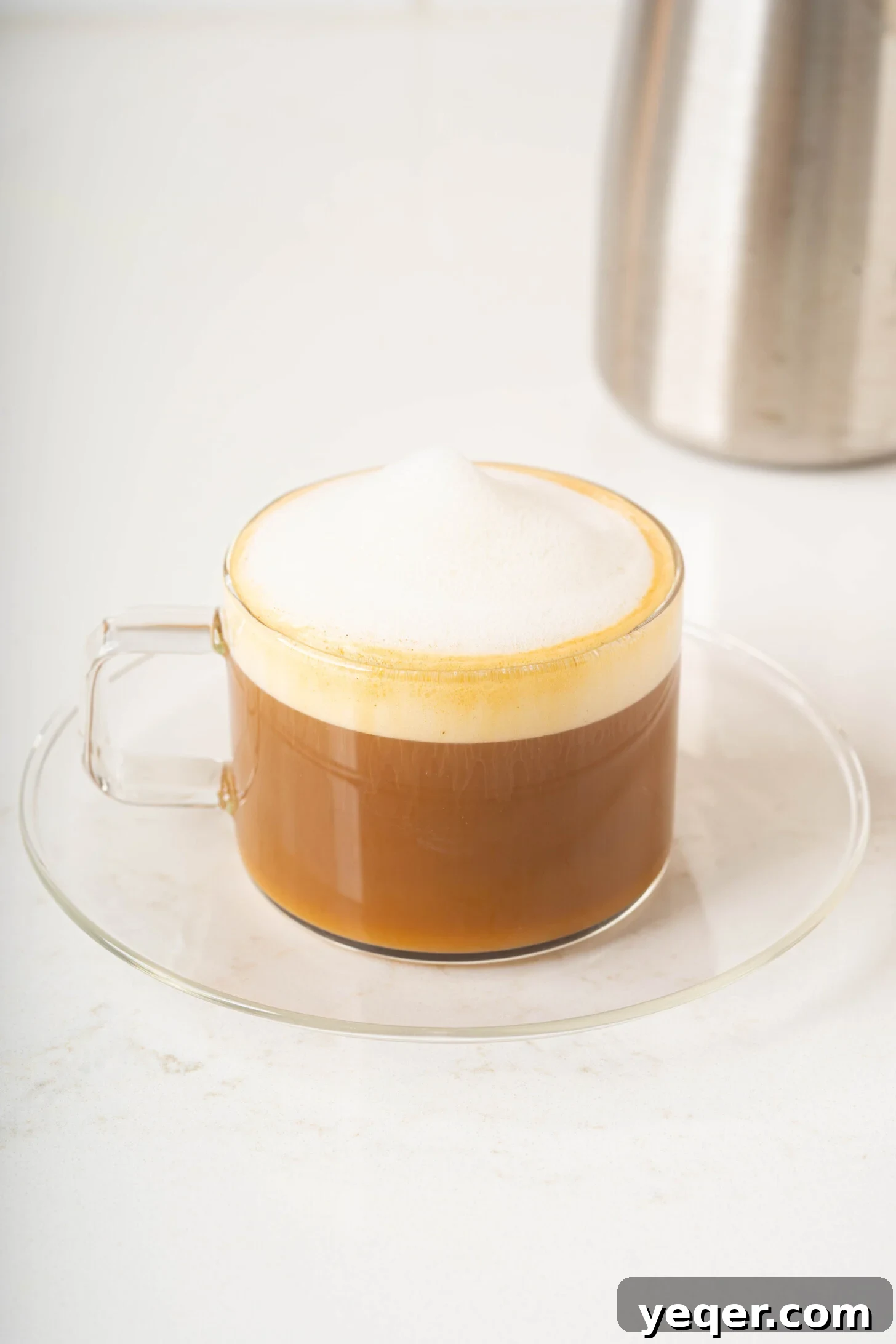 Your 10-Minute Cortado Perfect 1:1 Espresso and Steamed Milk 9 A perfectly made Cortado in a small, clear glass on a rustic wooden surface, highlighting its elegant layers and inviting warmth.