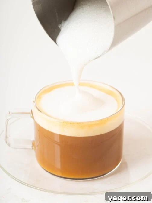 A creamy smooth Spanish Cortado in a small glass, with a perfect balance of espresso and steamed milk, garnished with a few coffee beans.
