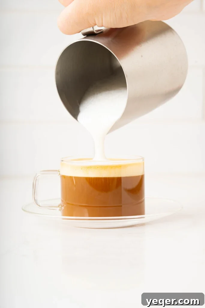 Your 10-Minute Cortado Perfect 1:1 Espresso and Steamed Milk 7 Steamed microfoamed milk being poured into a glass of espresso, showcasing the elegant merging of coffee and milk for a Cortado.