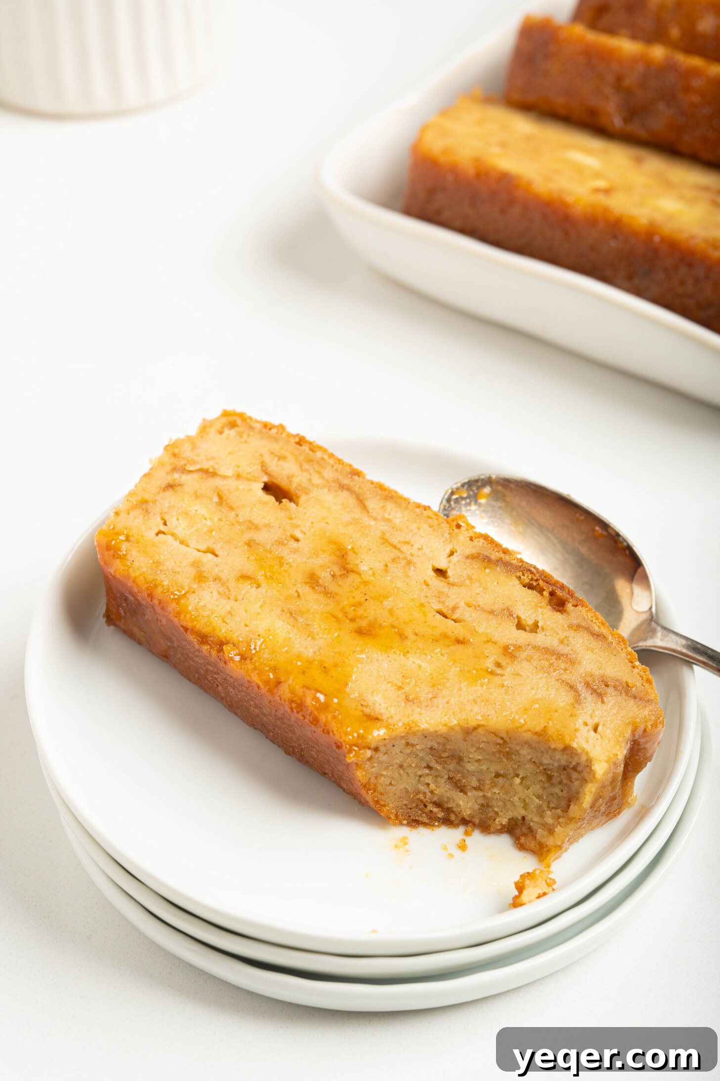 Puerto Rican Baked Bread Pudding 15 A close-up shot of a single slice of Puerto Rican Budin on a white plate, highlighting its moist interior and golden caramel.