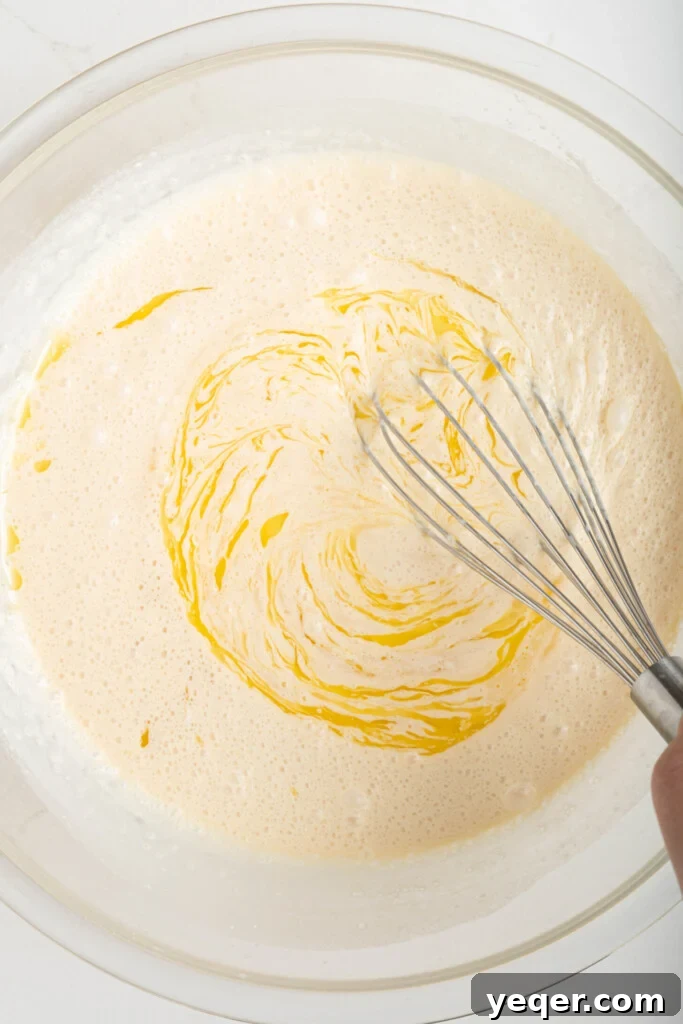 Puerto Rican Baked Bread Pudding 9 A whisk blending coconut milk, sweetened condensed milk, evaporated milk, melted butter, eggs, vanilla extract, cinnamon, and salt in a large bowl to form the smooth wet batter for budin.