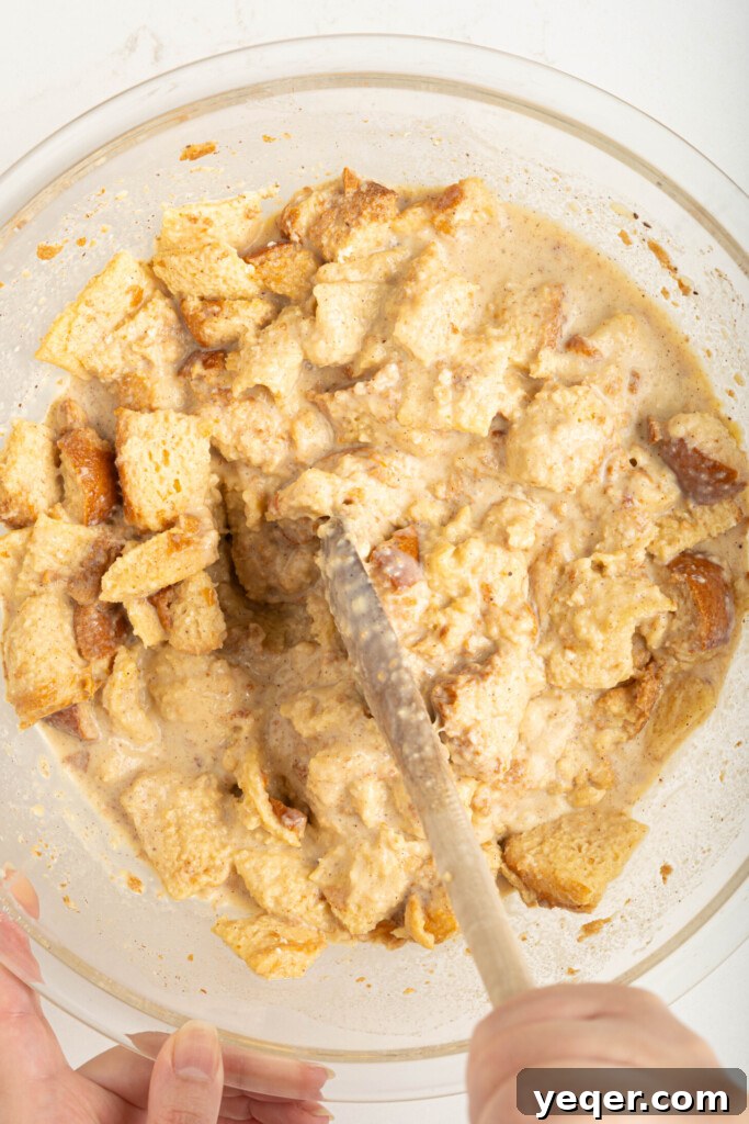 Puerto Rican Baked Bread Pudding 10 A spoon mixing the cubed bread into the wet budin batter, mashing it to achieve a smooth and creamy consistency.