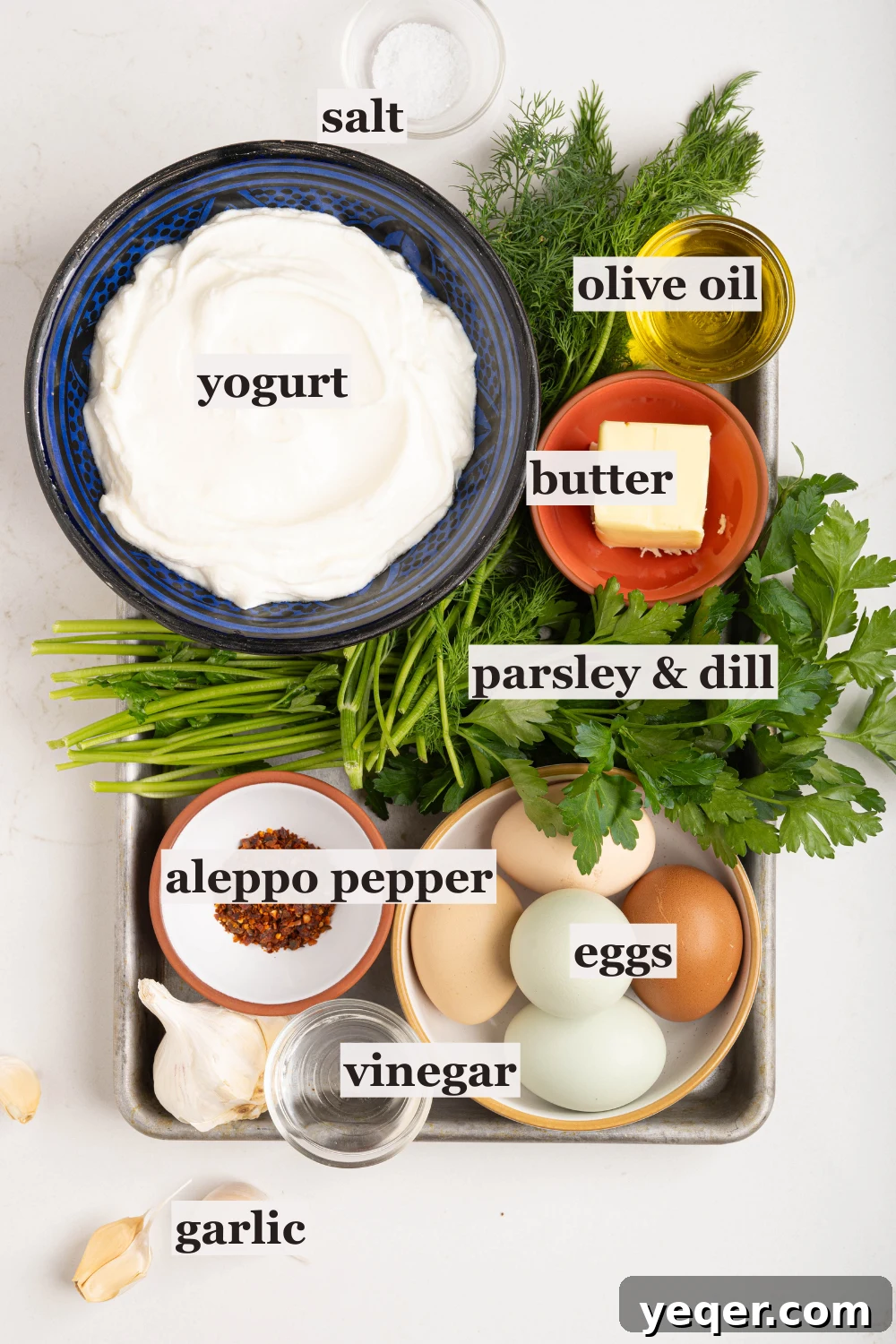 30-Minute Cilbir Turkish Eggs with Creamy Yogurt 3 Bowls of fresh ingredients for Turkish eggs, including Greek yogurt, olive oil, vinegar, butter, and various fresh herbs.