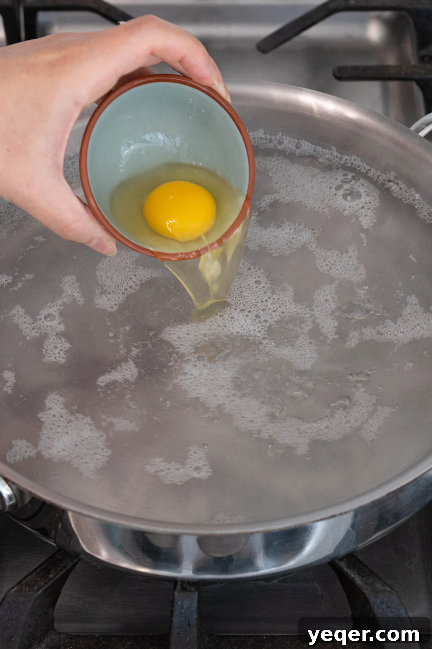 30-Minute Cilbir Turkish Eggs with Creamy Yogurt 8 A close-up of a fresh egg being carefully poured into a pot of simmering water for poaching.