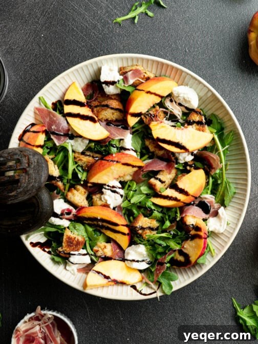Burrata peach salad in a white bowl with salad spoons, ready for serving.