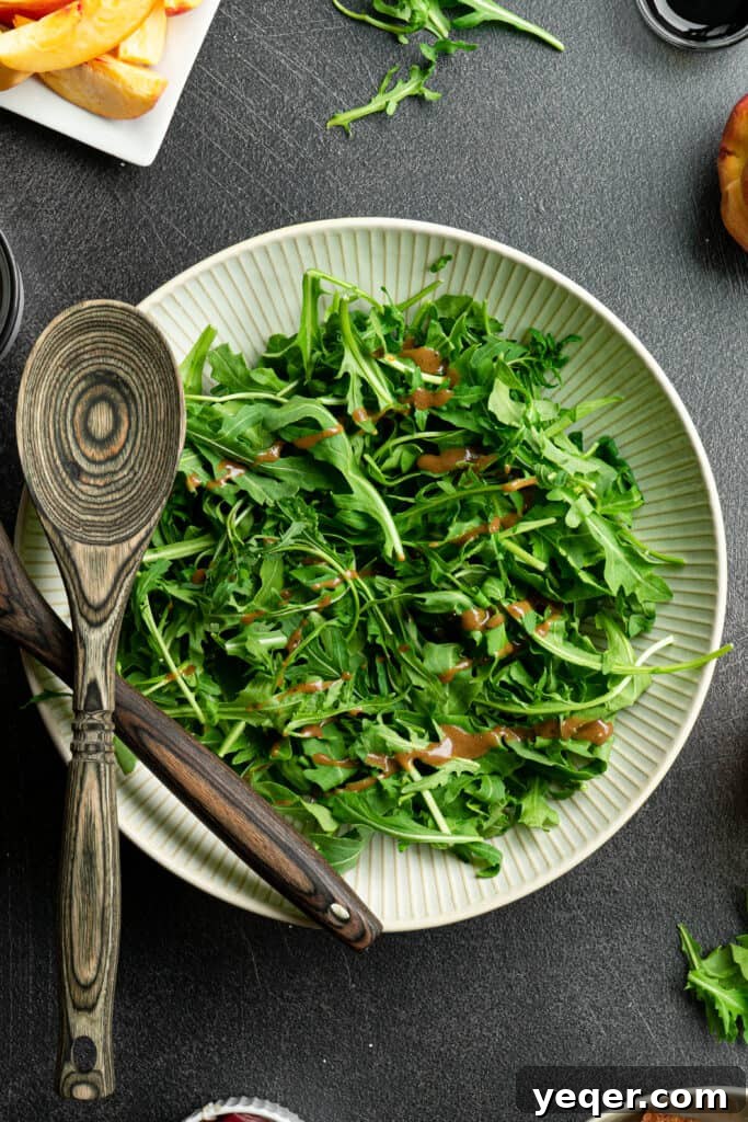 Decadent Peach Prosciutto Burrata Salad with Arugula and Crispy Croutons 4 Arugula with dressing in a large white salad bowl, ready for toppings.