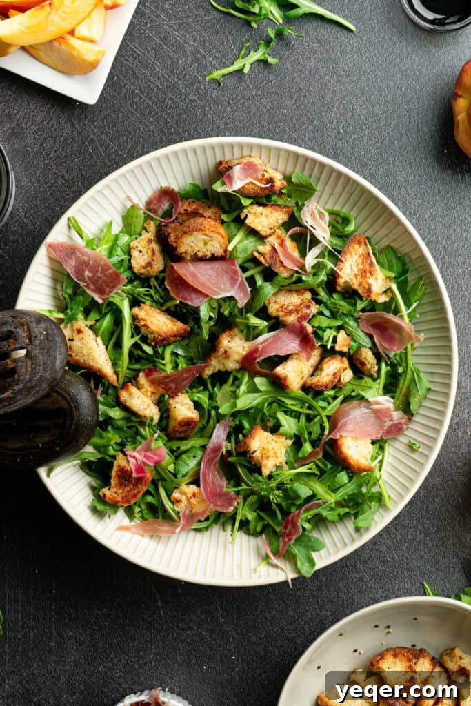 Decadent Peach Prosciutto Burrata Salad with Arugula and Crispy Croutons 6 Arugula with prosciutto, croutons, and dressing in a large white salad bowl, adding the savory element.