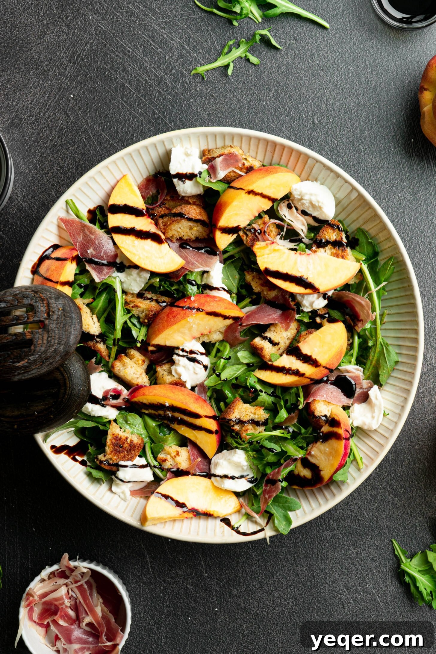 Decadent Peach Prosciutto Burrata Salad with Arugula and Crispy Croutons 10 Close-up of burrata peach salad in a white bowl with salad spoons, highlighting the burrata.